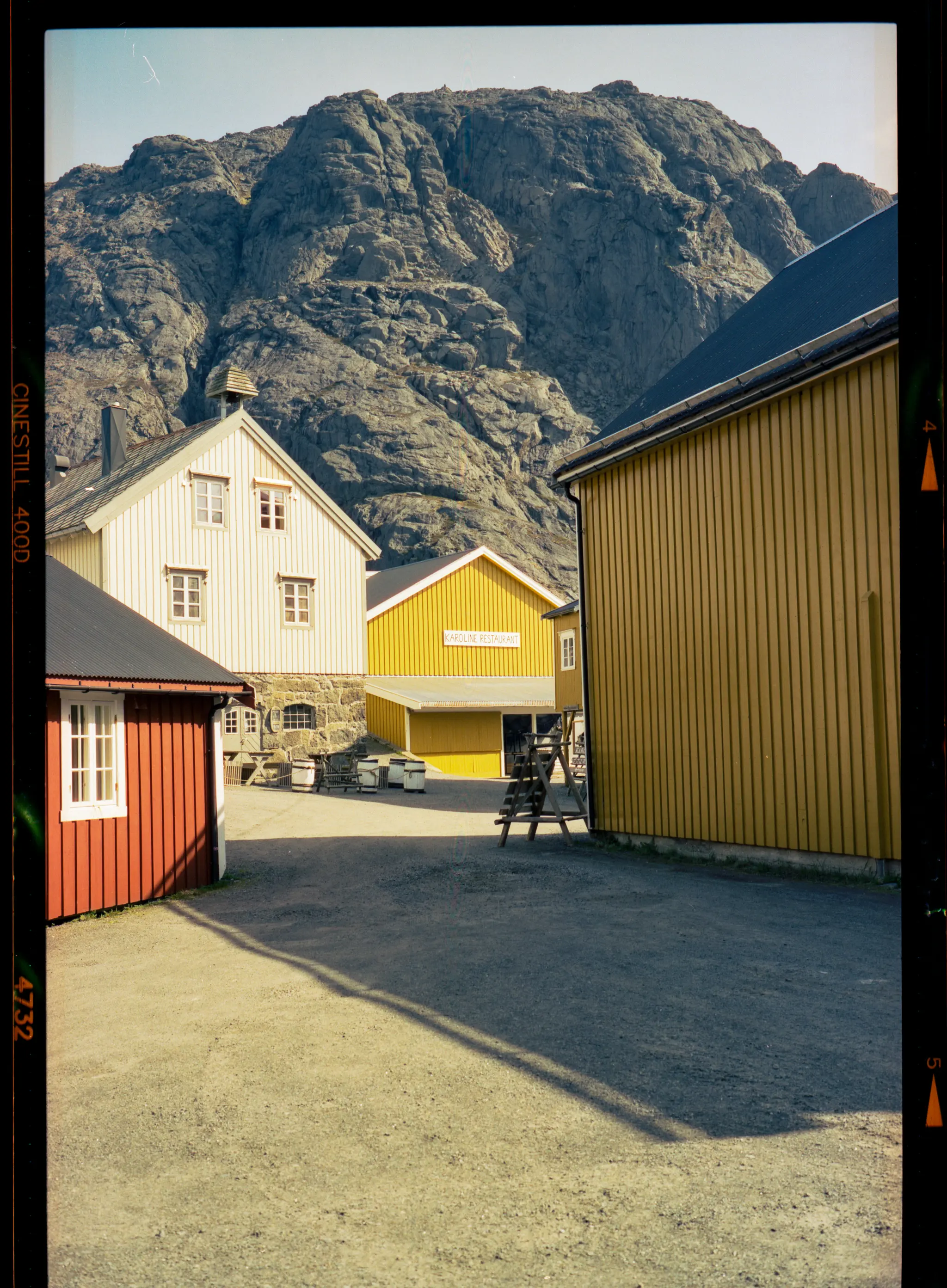 A yellow warehouse and red cabin below a grey rock face