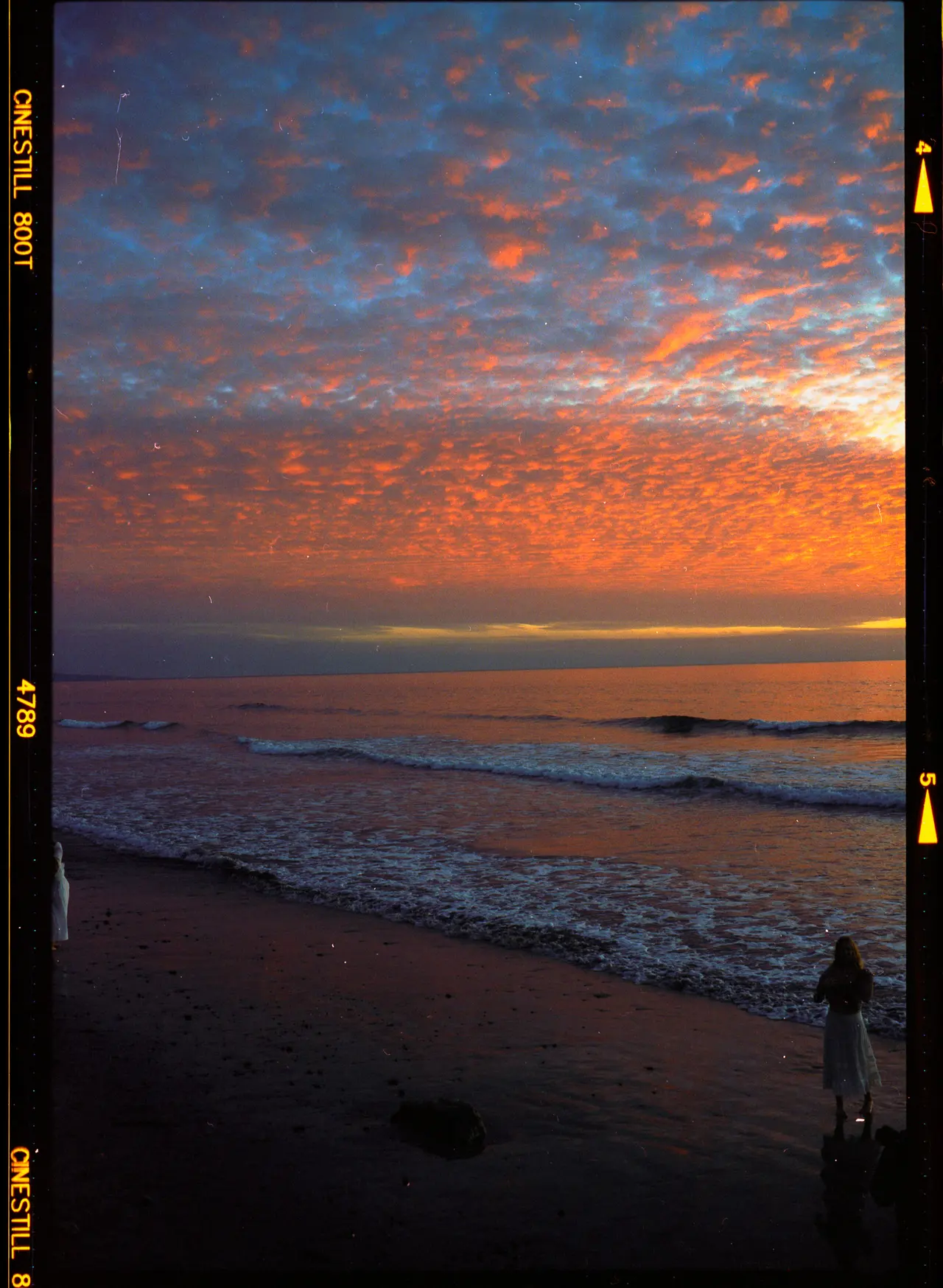 Mackerel clouds lit orange over a Carlsbad beach at dusk