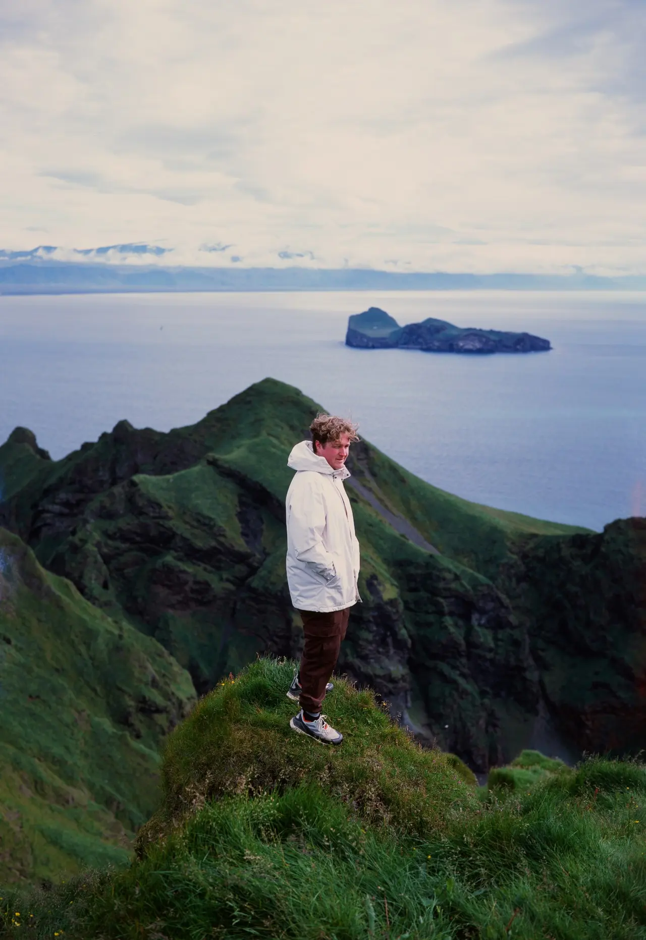 A hiker on a grassy peak above the sea, an island visible offshore