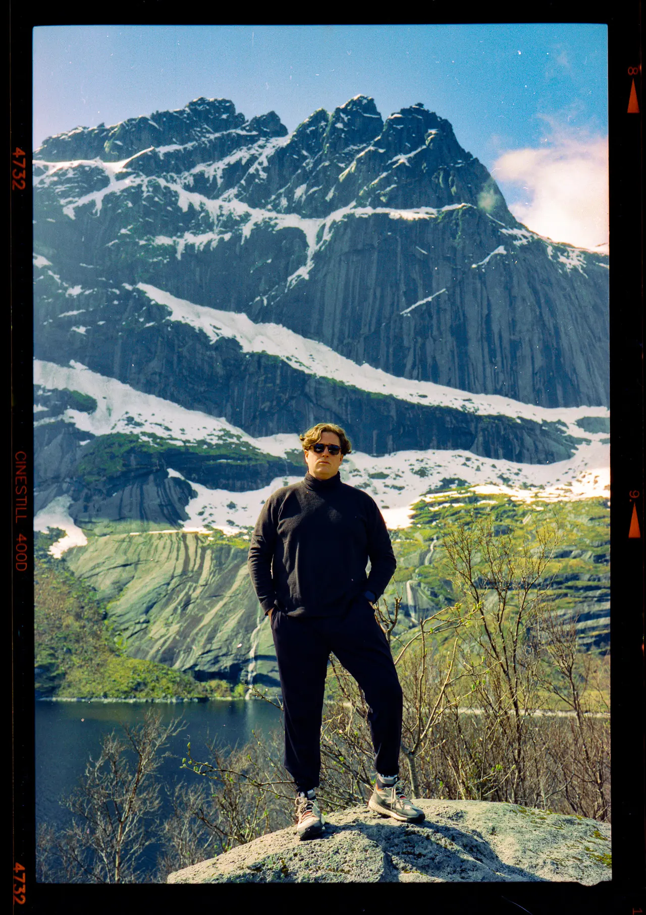 A figure on a rock outcrop with snow-streaked peaks behind